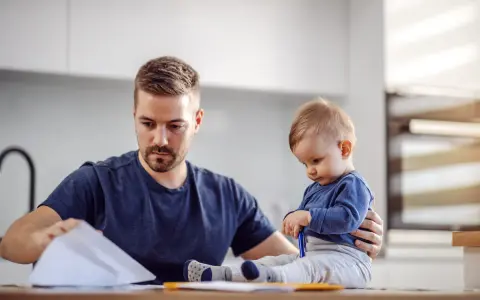 Ojciec pracuje w domu, a dziecko siedzi obok, bawiąc się długopisem. To obraz codziennych kontaktów z dzieckiem w miejscu zamieszkania matki.