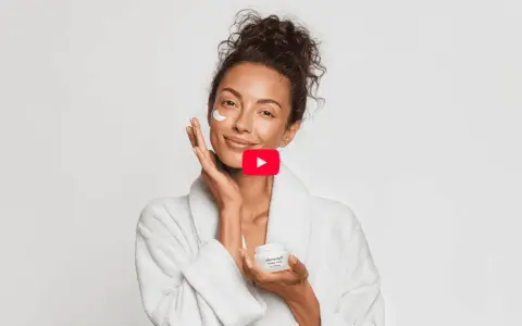 Donna sorridente applica crema viso, un gesto di skincare semplice per una pelle radiosa.