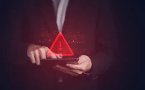 Czerwony trójkąt z wykrzyknikiem nad tabletem, symbolizujący groźbę karalną w cyfrowym świecie.