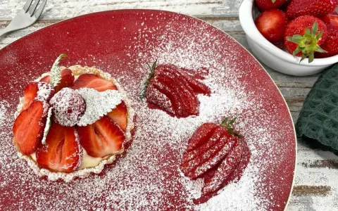 Zuckersüße Erdbeer Tartelettes, bestäubt mit Puderzucker, auf rotem Teller. Daneben frische Erdbeeren und eine Gabel.
