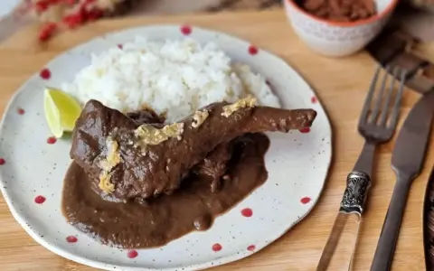 Un delicioso conejo guisado en mole oscuro, servido con arroz blanco y una rodaja de limón.