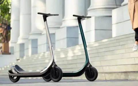 Deux trottinettes électriques modernes, idéales pour votre application trajet trottinette. L'une argentée, l'autre vert émeraude, sur des marches devant des colonnes.