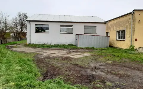 Teren wokół budynków jest nierówny, z błotnistymi śladami i trawą. Widać tu różne formy terenu, od płaskich placów po lekko nachylone trawniki.