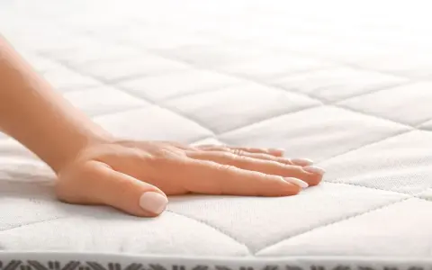 Main d'une femme effleurant un matelas orthopédique, offrant un confort et un soutien idéaux pour un sommeil réparateur.