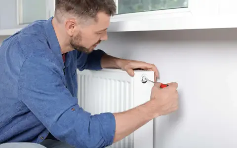 Mężczyzna używa śrubokręta, by odpowietrzyć grzejnik. To prosty sposób na pozbycie się powietrza z instalacji.