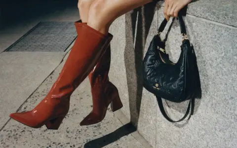 Kobieta w czerwonych kozakach i pikowanej torebce z logo Nine West. Nine West to znana marka obuwia i akcesoriów.
