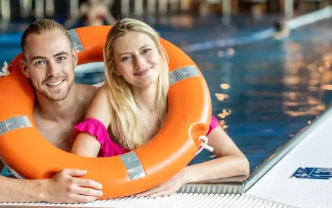 Uśmiechnięta para w basenie, trzymająca koło ratunkowe. Idealny weekend z przyjaciółką, pełen relaksu i zabawy w wodzie.