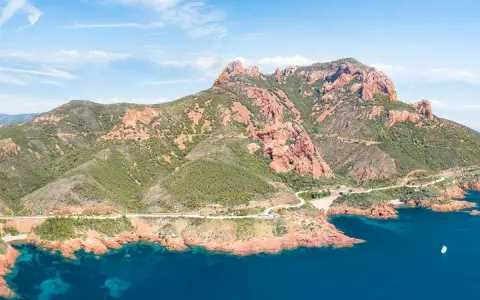 Strada panoramica sulla Corniche de l'Esterel, con montagne rosse e mare blu intenso.