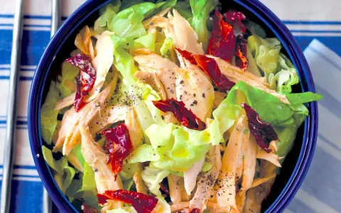 Insalata di pollo lesso con lattuga croccante e pomodori secchi, condita con pepe nero macinato.