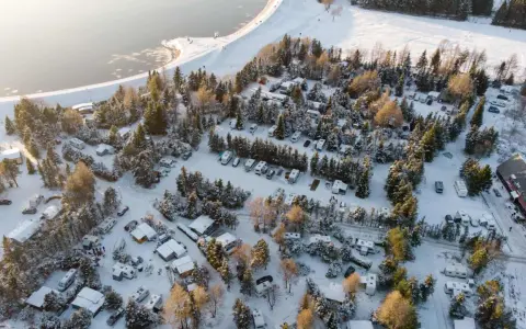 Wintercamping im Erzgebirge: Wohnmobile und Wohnwagen stehen im Schnee auf einem Campingplatz am See, umgeben von verschneiten Bäumen.