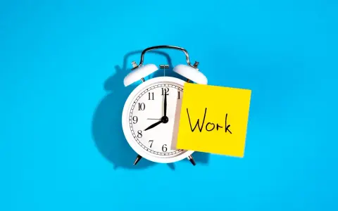 Reloj despertador blanco con nota amarilla que dice "Work", recordando la importancia de la jornada laboral.