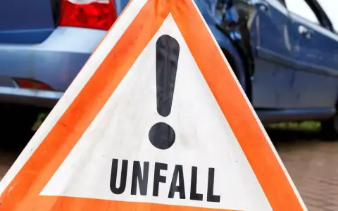 Warnschild "Unfall" vor beschädigtem Auto. Nach einem Verkehrsunfall kann eine Vorstandsbeschwerde bei der Versicherung nötig sein.