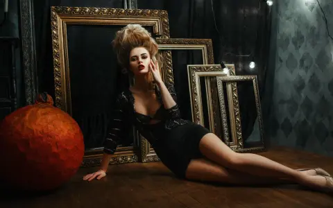 Une femme aux cheveux volumineux, dans une robe noire, pose près de cadres dorés. Un tuto Photoshop pour un look dramatique.