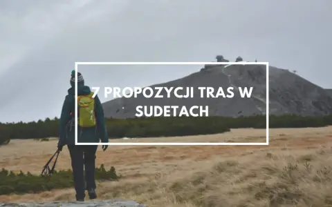 Turystka z plecakiem i kijkami maszeruje przez trawiaste tereny w Sudetach, zmierzając ku górze z budynkami.