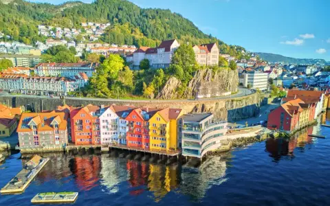 Kolorowe domy nad wodą w Bergen, idealne na norwegia zwiedzanie. W tle wzgórza porośnięte drzewami.