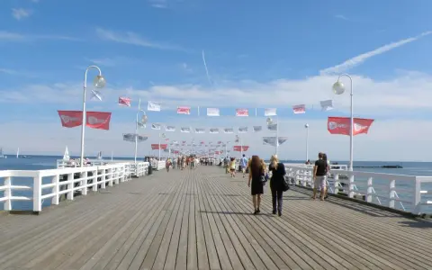 Spacer po najdłuższym molo w Polsce. Ludzie przechadzają się pod biało-czerwonymi flagami i błękitnym niebem.