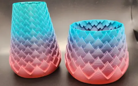 Two dragon-scale patterned vases, created with color 3d printing, showcase a gradient from coral pink to teal blue.
