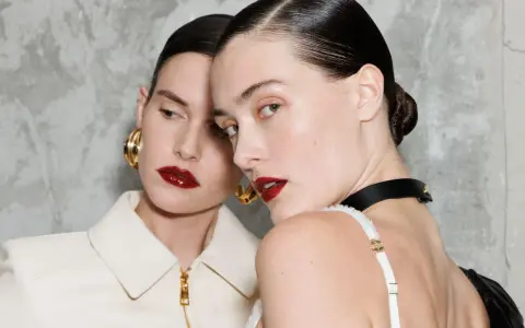 Due modelle con labbra audaci e un intenso colore rossetto, con capelli tirati indietro e orecchini dorati.
