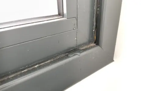 Gotas de lluvia resbalan por el marco de una ventana gris, dejando un rastro húmedo.