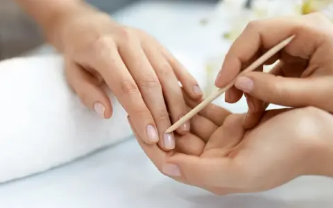 Delikatne dłonie poddawane są zabiegowi manicure biologicznego. Drewniany patyczek delikatnie odsuwa skórki, przygotowując paznokcie do dalszych pielęgnacji.