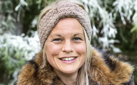 Glad kvinna med virkat pannband med twist och pälskrage, ute i naturen.