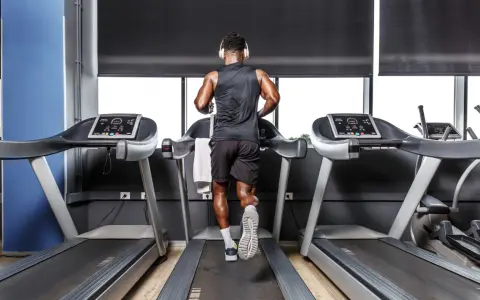Mann mit Kopfhörern absolviert ein intensives Laufband Training in einem modernen Fitnessstudio.