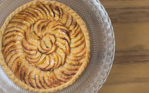 Tarte aux pommes dorée sur pâte feuilletée, disposée en spirale sur un plat en verre gravé. Un délice croustillant.