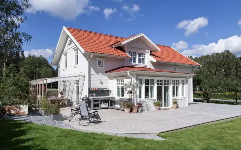 Vitt hus med rött tak och stor altan. Perfekt för att behandla altan och njuta av sommaren.