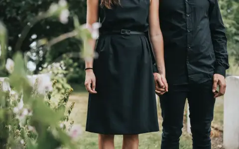 Frau in schwarzem Kleid und Mann in schwarzer Kleidung halten Händchen. So zieht man zur Beerdigung an als Frau.