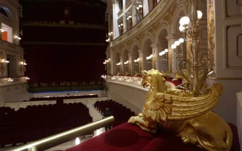 Interno del Teatro Galli di Rimini, con poltrone rosse, palchi dorati e una sfinge alata in primo piano.