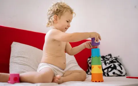 Chłopiec, 3 latek, nie mówi, ale wszystko rozumie. Z uśmiechem układa kolorowe kubeczki na łóżku.