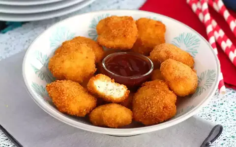 Un plato lleno de crujientes nuggets caseros, listos para mojar en salsa barbacoa.