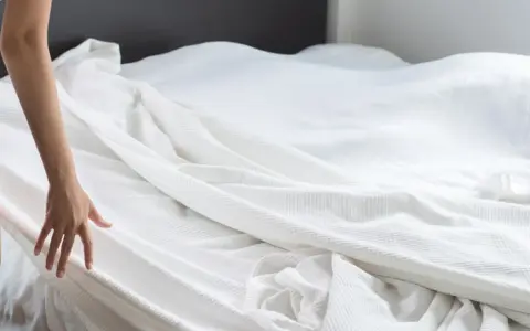 Dłoń kobiety sięga do białej pościeli, przygotowując się do zadania, jak założyć poszewkę na kołdrę.