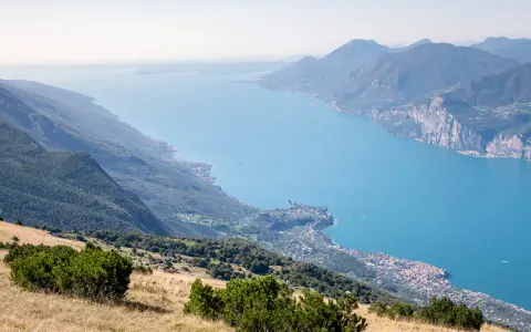 Panoramica mozzafiato del lago di Garda sponda veronese, con montagne verdi e un borgo pittoresco affacciato sull'acqua azzurra.