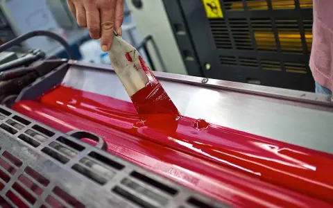Mano esparciendo tinta roja en rodillos de imprenta, mostrando las ventajas de la imprenta para la difusión masiva de información.