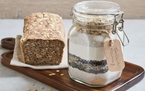 Selbstgemachte brotbackmischung im Glas, bereit zum Backen. Daneben ein frisch gebackenes Brot mit Haferflocken und Körnern.