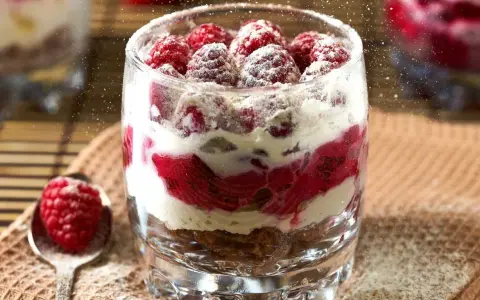 Pyszne desery w pucharkach z malinami i kremem, posypane cukrem pudrem. Idealne na letnie popołudnie.