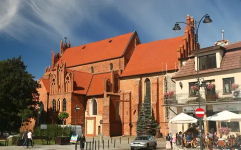Gotycka ceglana bazylika w Tczewie, z pomarańczowym dachem, to jedna z głównych atrakcji miasta. W tle kawiarniany ogródek.