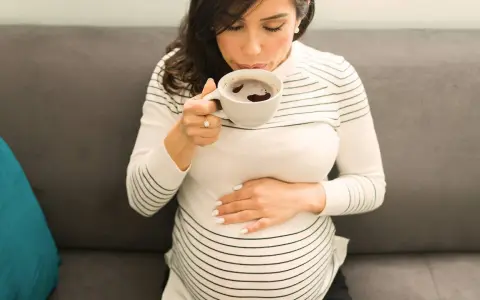 Schwangere Frau trinkt eine Tasse entkoffeinierten Kaffee, während sie ihren Bauch streichelt.