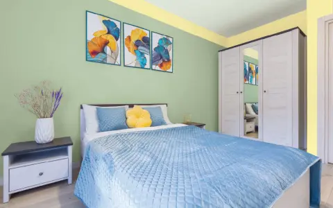 Dormitorio con paredes verde menta y detalles amarillos en el techo. Cama azul, mesita de noche y armario blanco. Inspiración de colores para pintar un dormitorio pequeño.