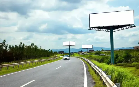 Pusta reklama przy drodze na terenie prywatnym, z widokiem na zakrzywioną autostradę i zielone wzgórza.