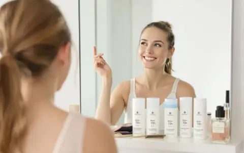 Uśmiechnięta kobieta w łazience, przed lustrem, z produktami "Bloker 72h" - najskuteczniejszy bloker potu.