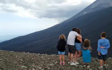 Famiglia in vacanza in Sicilia con bambini, ammira il pendio scuro di un vulcano.