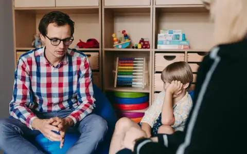 Terapeuta rozmawia z dzieckiem, ćwicząc teorię umysłu. W tle zabawki i pomoce edukacyjne.