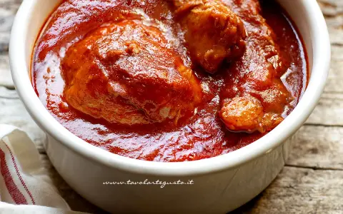 Un saporito ragù napoletano in una ciotola bianca, con pezzi di carne succulenta immersi nel sugo rosso intenso.