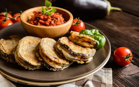Cotolette di melanzane dorate e croccanti, servite con salsa di pomodoro e basilico fresco.