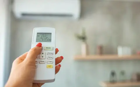 Mano con control remoto de aire acondicionado, ajustando el modo dry para dormir. La pantalla muestra 25°C.