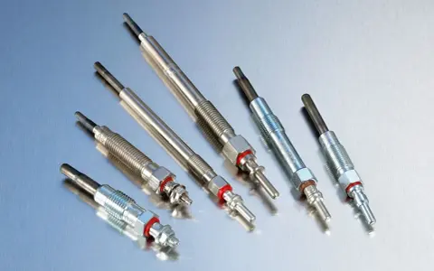 Sześć świec żarowych, kluczowych elementów silnika diesla, leży na metalicznej powierzchni.