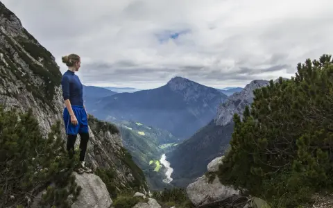 Donna in cima a una montagna, contemplando un vasto paesaggio alpino. Il vero hiking significato è nella libertà e nella vista mozzafiato.