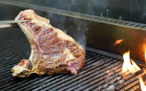 Una succulenta bistecca alla fiorentina, con la sua storia di sapori, cuoce sulla griglia tra fiamme vive e fumo.